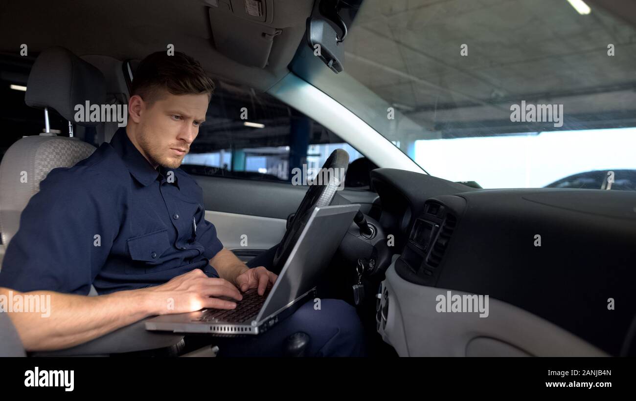 Agent de police de sexe masculin travaillant sur ordinateur portable en voiture, le remplissage des données dans le rapport de la criminalité Banque D'Images