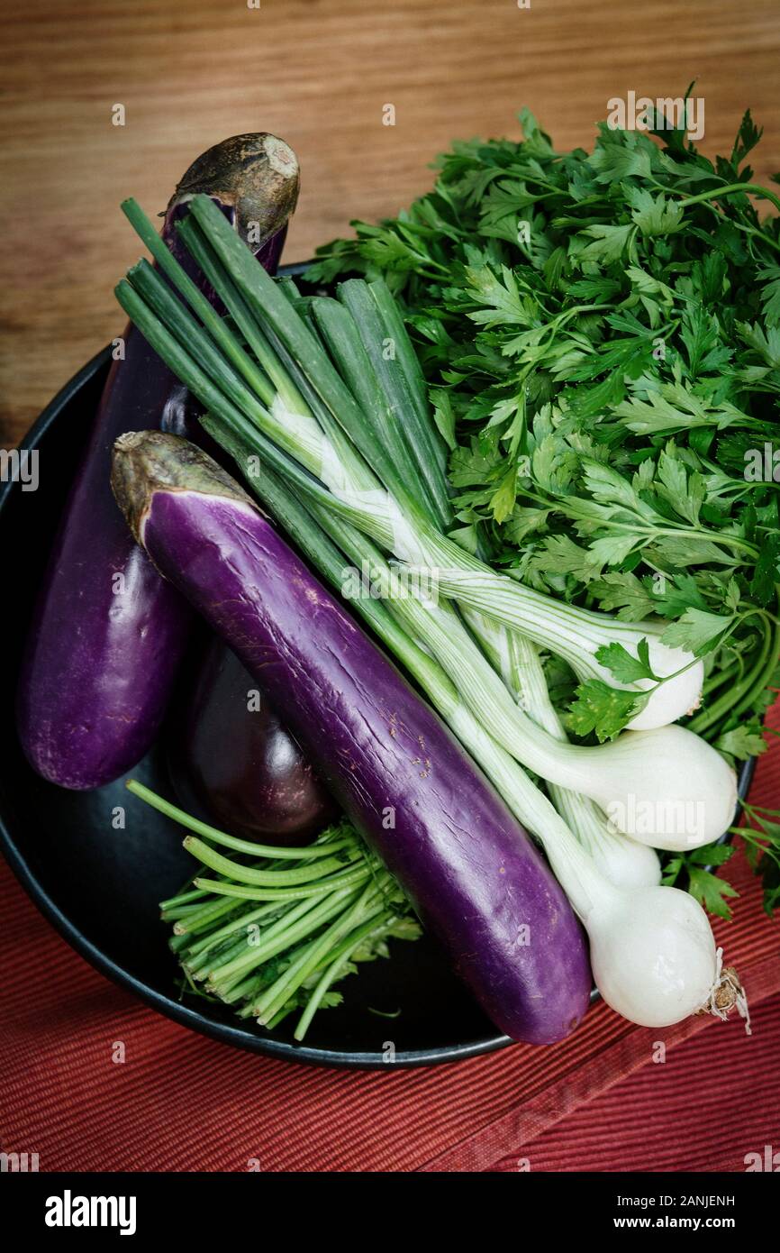 Légumes biologiques rustiques, enveloppés dans du papier sur un fond en bois. Aubergine, oignons de printemps et coriandre dans un bol Banque D'Images