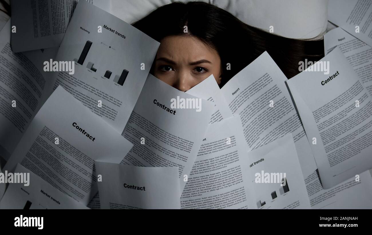 Femme couverte de pile de documents au lit, la surcharge de travail concept Banque D'Images