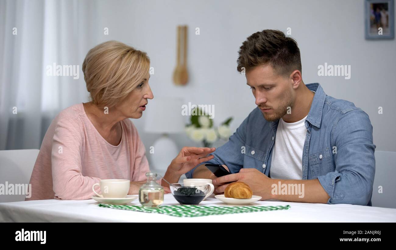 Mère inquiète de parler à son fils adulte infantile à jouer aux jeux vidéo sur smartphone Banque D'Images