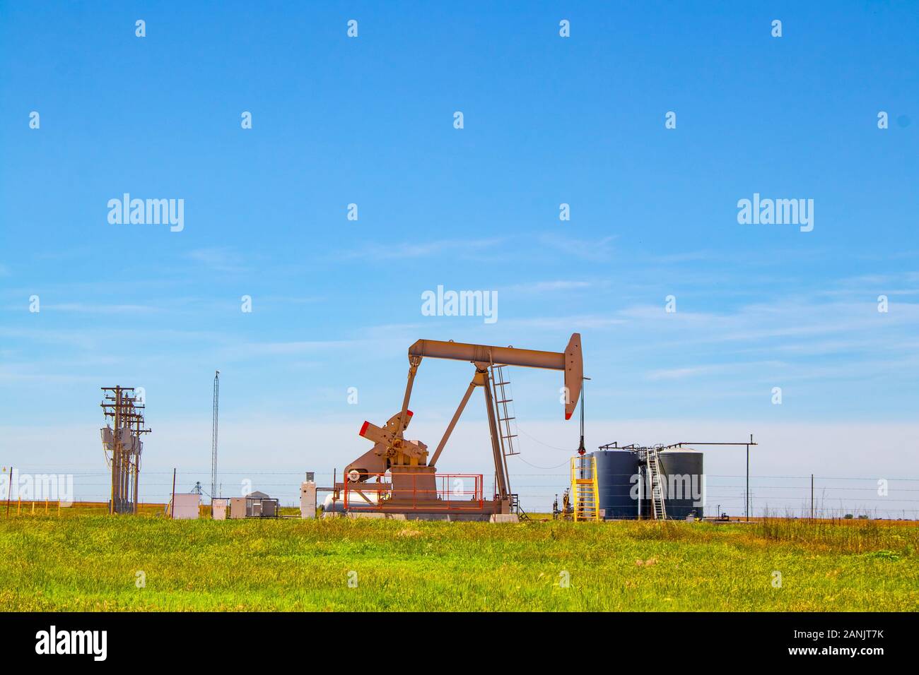 Pompe de travail Jack sur puits d'huile avec des réservoirs sur place à l'horizon sur les plaines avec lignes électriques et ciel bleu en arrière-plan Banque D'Images