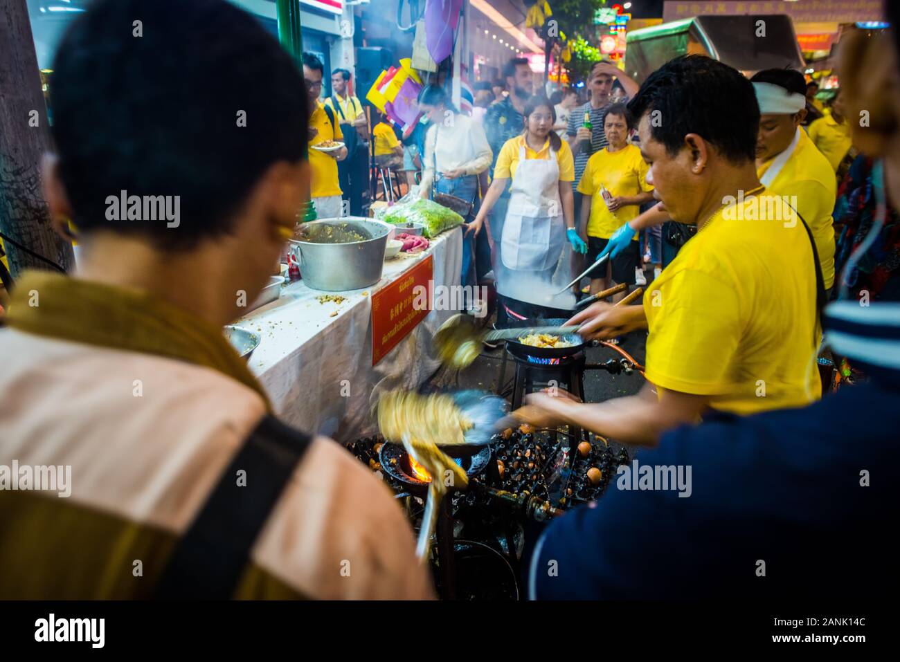 Bangkok/Thaïlande-05December2019: Célébration de nuit sur la rue de l'anniversaire du roi Bhumibol où les cuisiniers préparent la nourriture dans des chemises jaunes typiques Banque D'Images
