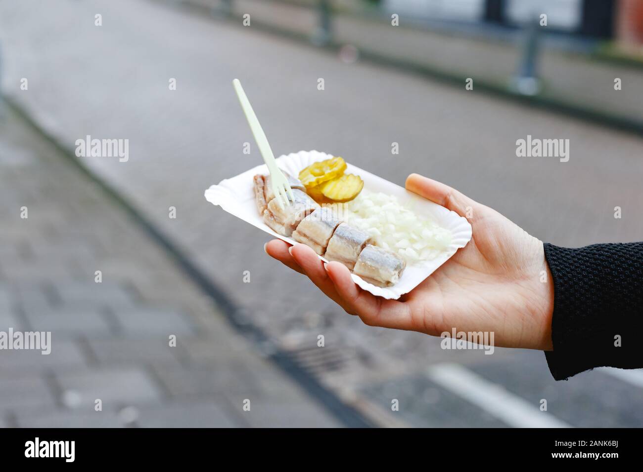 Poisson hareng Holland main de femme en extérieur. L'alimentation de rue traditionnel néerlandais, le hareng poisson. Stock photo street food, hareng poisson avec oignons et cornichons Banque D'Images