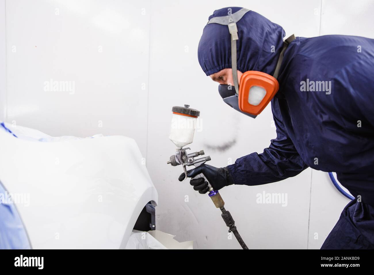 Travailleur en bleu de travail avec un respirateur et lance à main dans la main dans la cabine de pulvérisation Banque D'Images