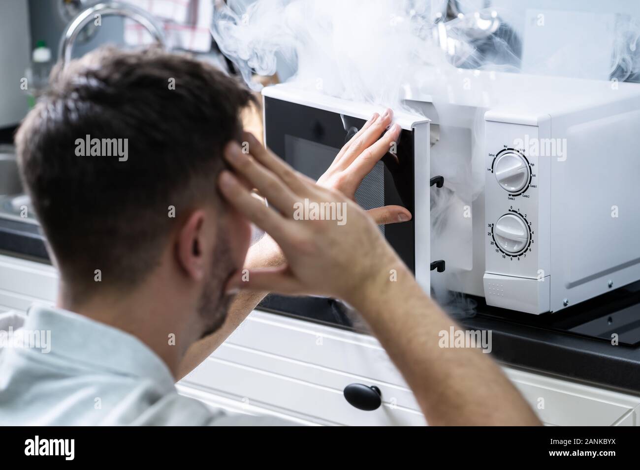 Jeune homme pulvérisant extincteur sur le four à micro-ondes dans la cuisine Banque D'Images