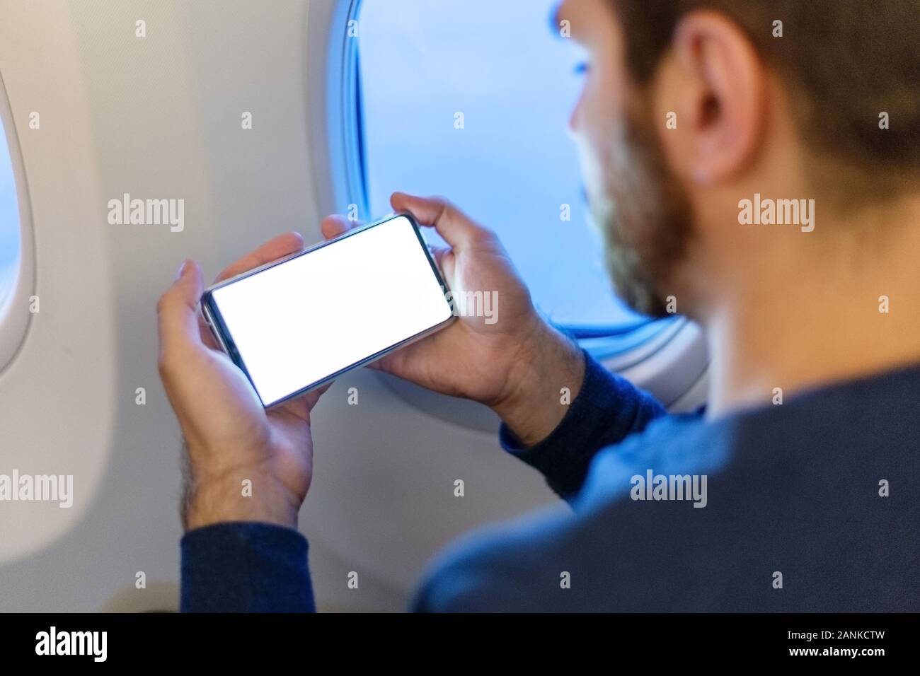 Smartphone maquette avion. Young man holding européen attrayant écran blanc smartphone dans les mains en avion. Maquette pour un jeu, application mobile Banque D'Images