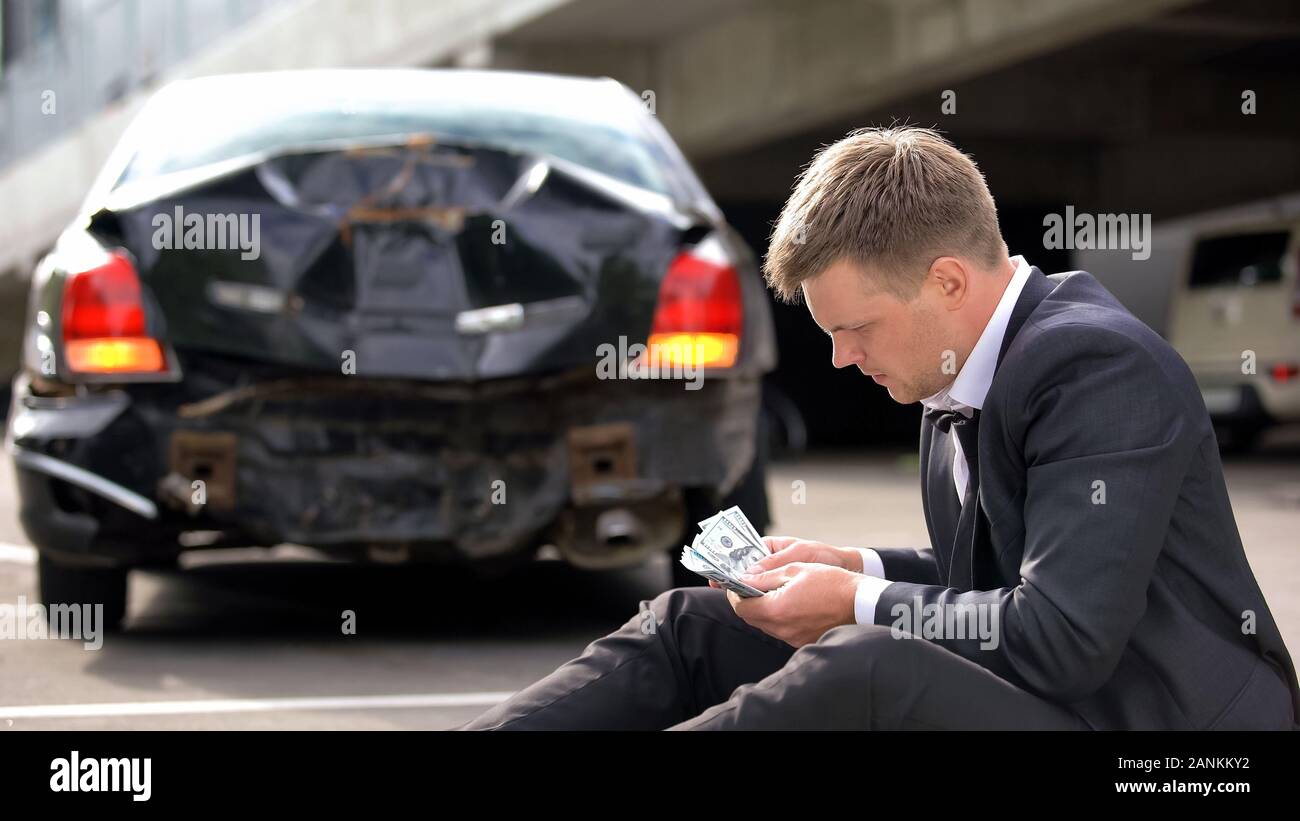Jeune homme compte dollars city road sur fond auto casse, accident de voiture Banque D'Images
