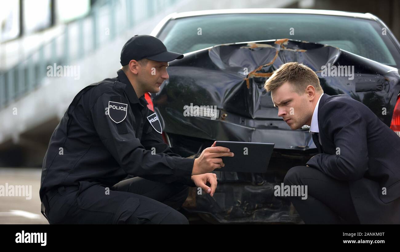 Agent de police montrant des photos à tablette conducteur accident de la scène, preuve Banque D'Images