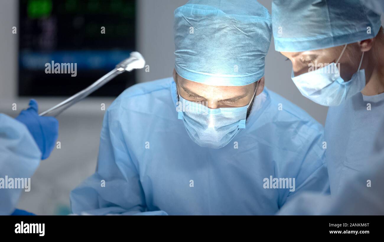 Chirurgien performing operation, sous-main tenant l'assurance-maladie, les outils médicaux Banque D'Images