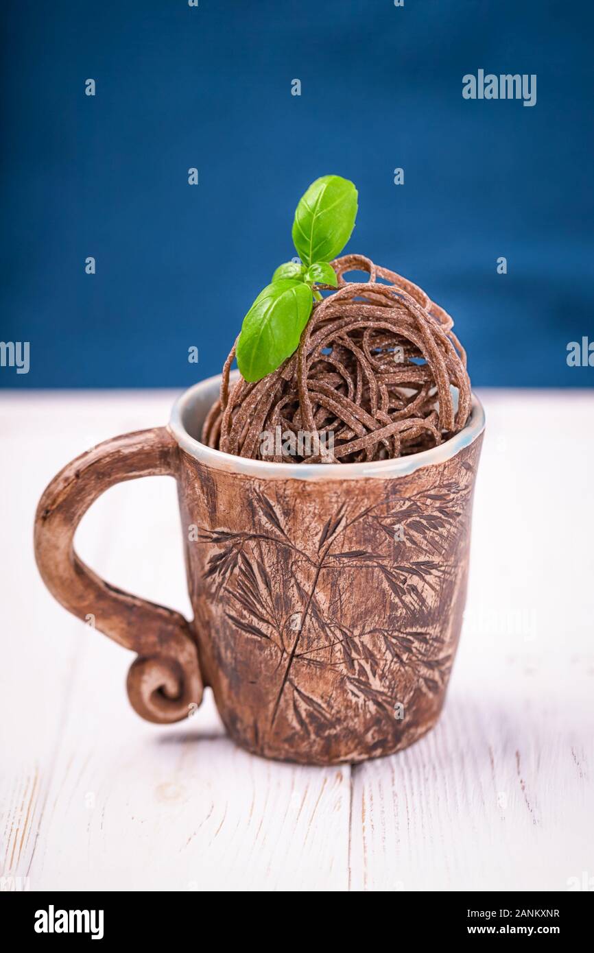 Les pâtes de sarrasin crus brun nouilles dans une tasse en céramique sur le classique fond bleu. Concept sans gluten. Copy space Banque D'Images