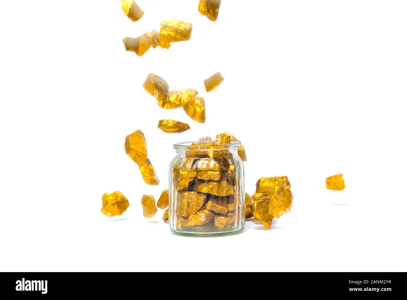 La chute des pépites d'or, le minerai d'or , pierre précieuse ou forfaitaire en pierres dorées et bocal verre isolé sur fond blanc. Banque D'Images