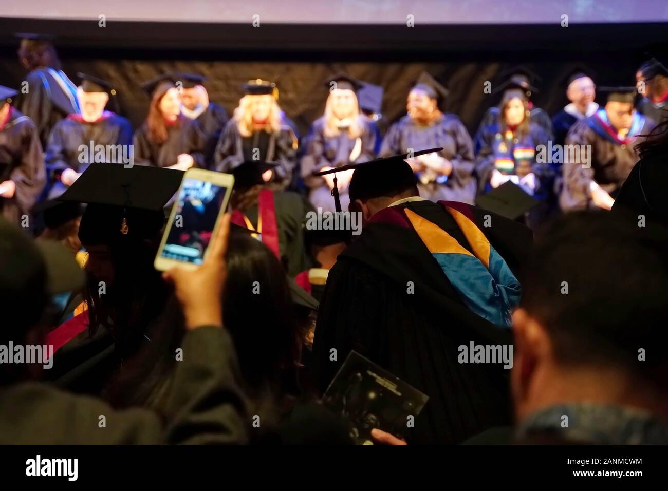 New York, NEW YORK / USA - Décembre 13, 2019 De : Grad habillés en cap and gown prend un siège devant la faculté et à l'avant de la foule des parents comme l'audien Banque D'Images