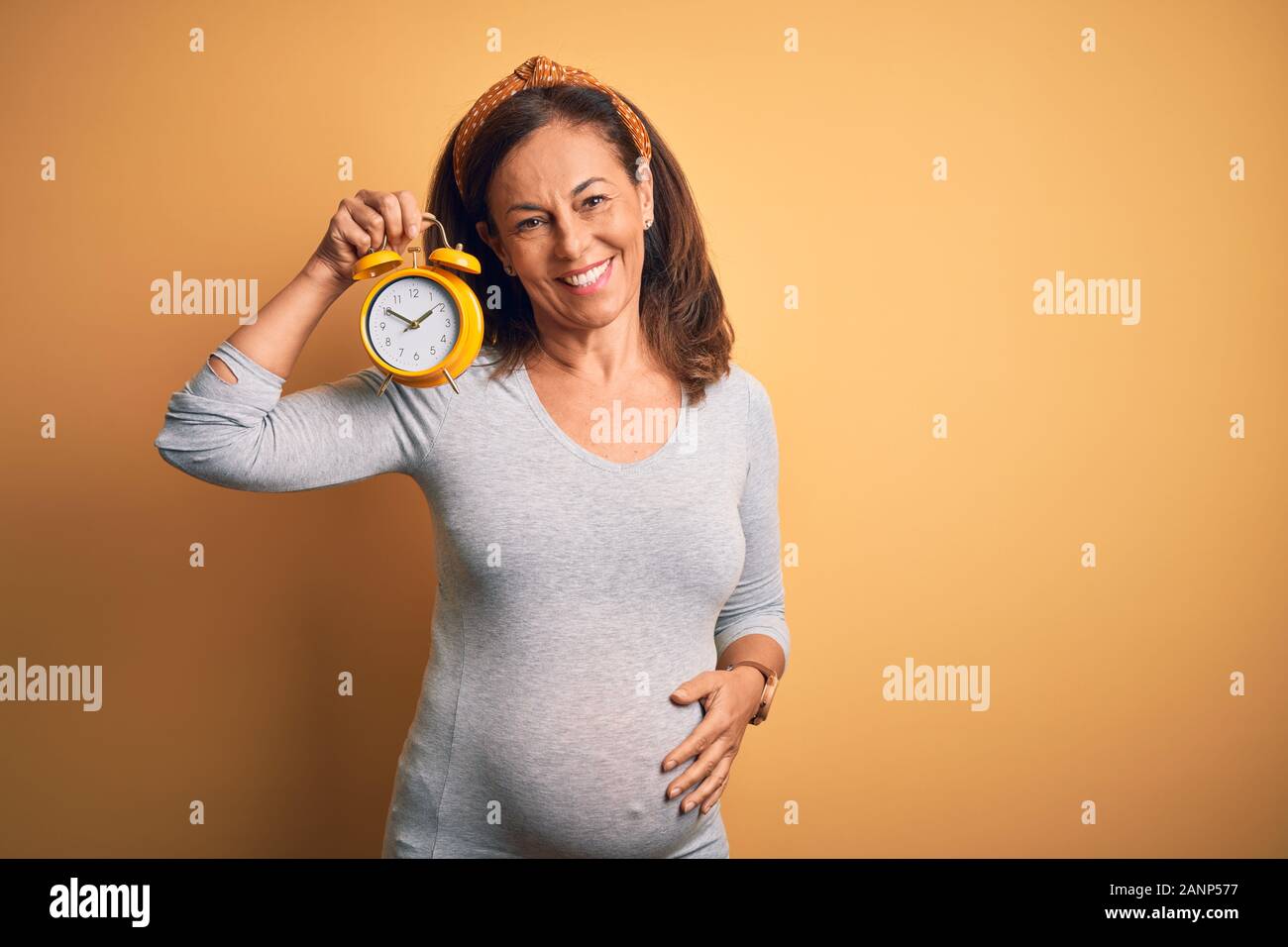 L Age Moyen Femme Enceinte Attend Bebe A L Age De La Grossesse Holding Reveil Avec Un Visage Heureux Et Souriant Debout Avec Un Sourire Confiant Montrant T Photo Stock Alamy