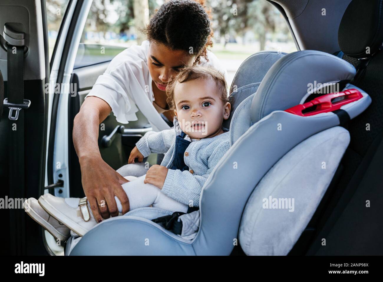 Little girl looking at camera while mère attacher les courroies sur siège de voiture de bébé Banque D'Images