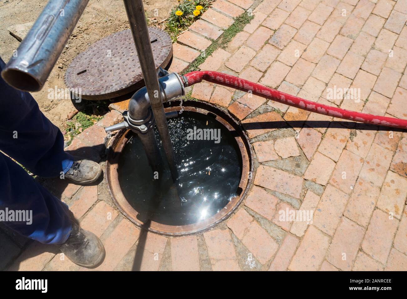 Employé, travailleur dans une couverture ouverte de trou d'homme débloquant un drain ou un égout bloqué avec tuyau de pression à Laingsburg, Afrique du Sud, concept de service public Banque D'Images