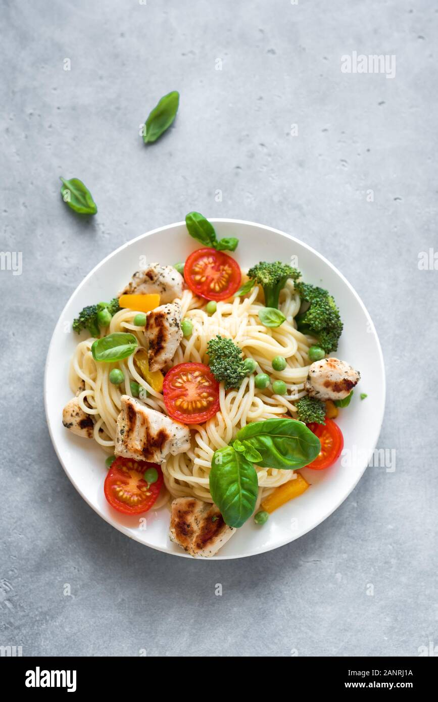 Pâtes Primavera poulet Spaghetti fait maison, un plat de pâtes avec du poulet, des légumes tomate, brocoli, pois verts, poivrons et les feuilles de basilic, haut Banque D'Images