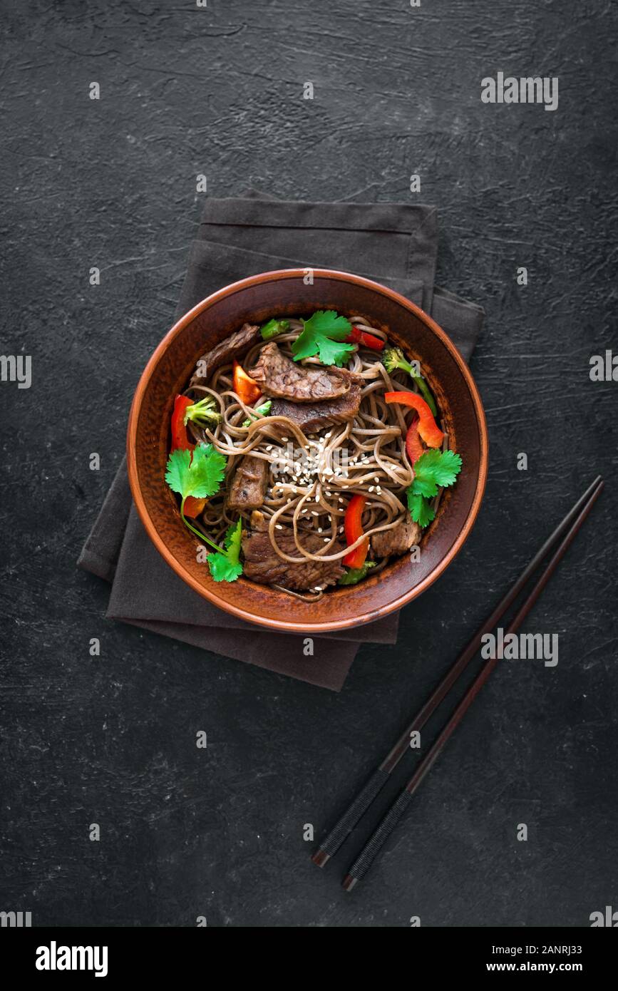 Les sautés avec nouilles soba, le boeuf (viande) et de légumes. La nourriture saine, de l'Asie repas sauté dans des bols sur fond noir, copiez l'espace. Banque D'Images