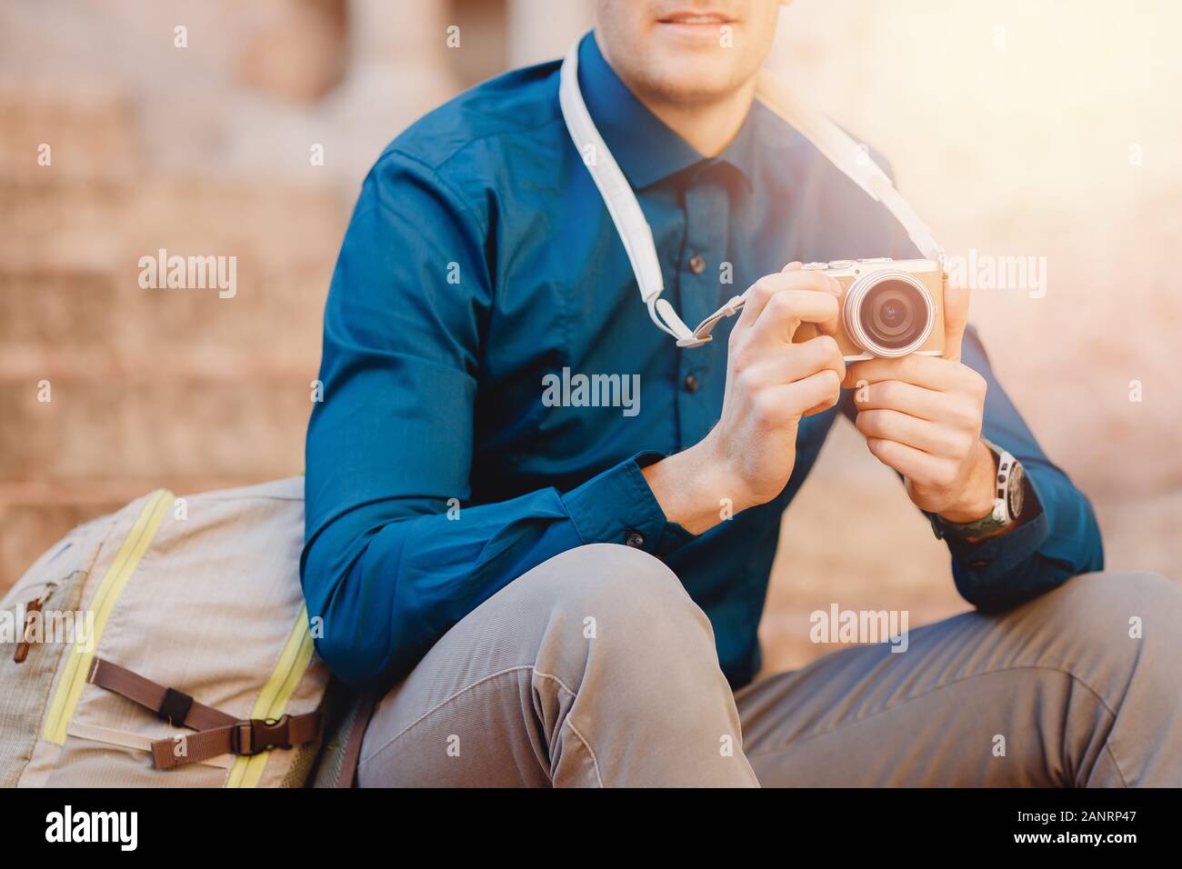 Photographe voyageur mâle avec petit appareil photo en mains, chemise bleue et son sac à dos Banque D'Images