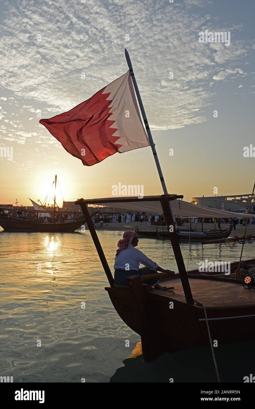 Les hommes assis sur le Dhow avec le drapeau du Qatar Katara au coucher du soleil, dhaw traditionnel festival, Doha, Qatar. Banque D'Images