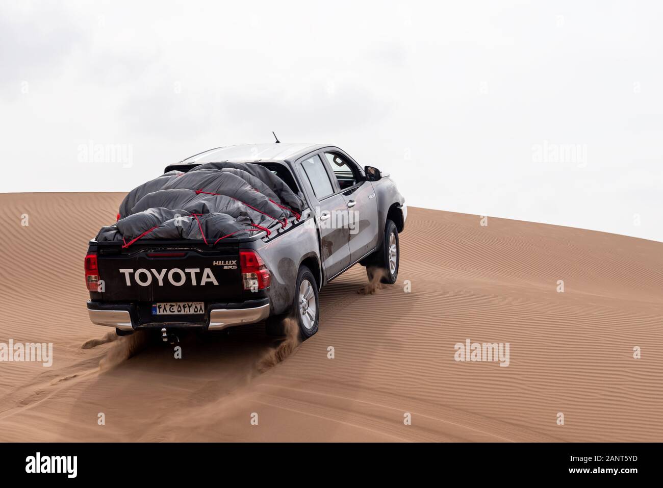 toyota hulux revo escalade une dune de sable éclaboussant des sables autour dans dasht e lut ou sahara désert Banque D'Images