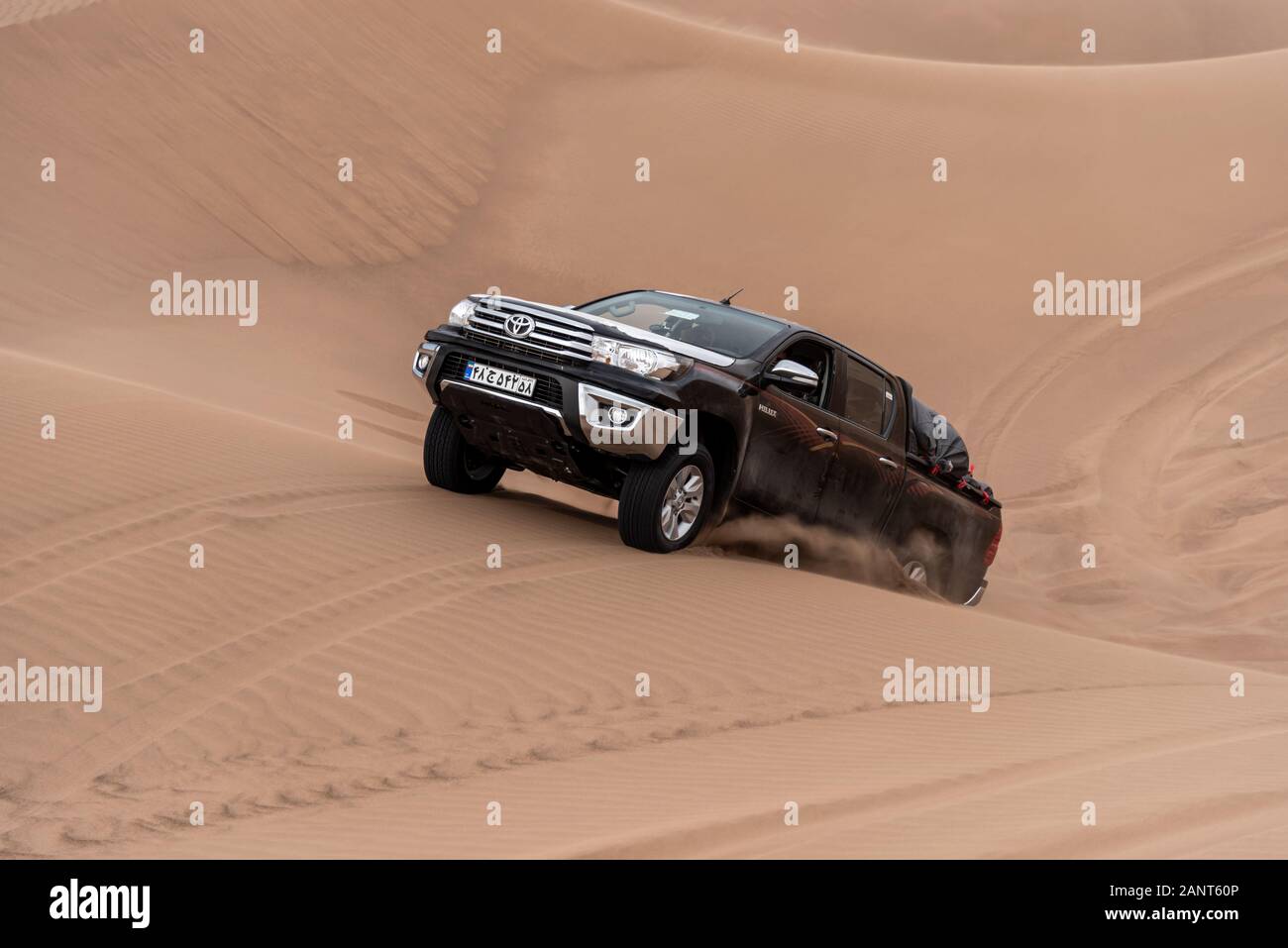 toyota hulux revo escalade une dune de sable éclaboussant des sables autour dans dasht e lut ou sahara désert Banque D'Images