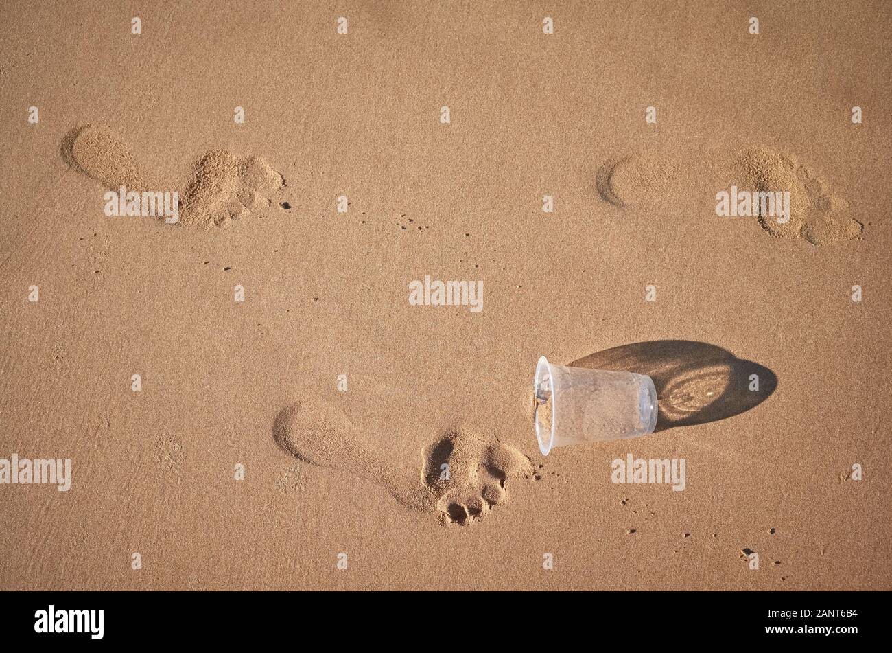 Empreintes et tasse en plastique sur une plage de sable fin, l'image conceptuelle. Banque D'Images