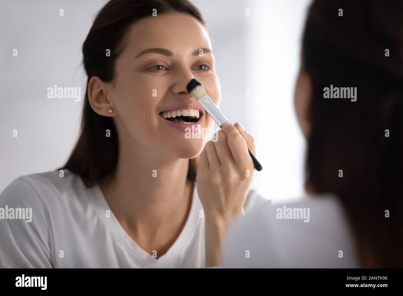 Smiling woman looking in mirror, appliquant le maquillage avec brosse Banque D'Images