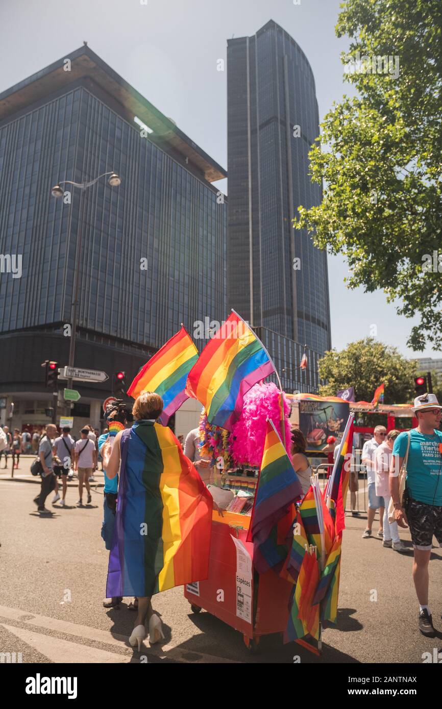 29 Juin 2019, Paris, France. Gay Pride Parade Day. Travestite devant un stand de goodies (drapeaux arc-en-ciel). Le skyskraper 'la Tour Montparnasse'. Banque D'Images