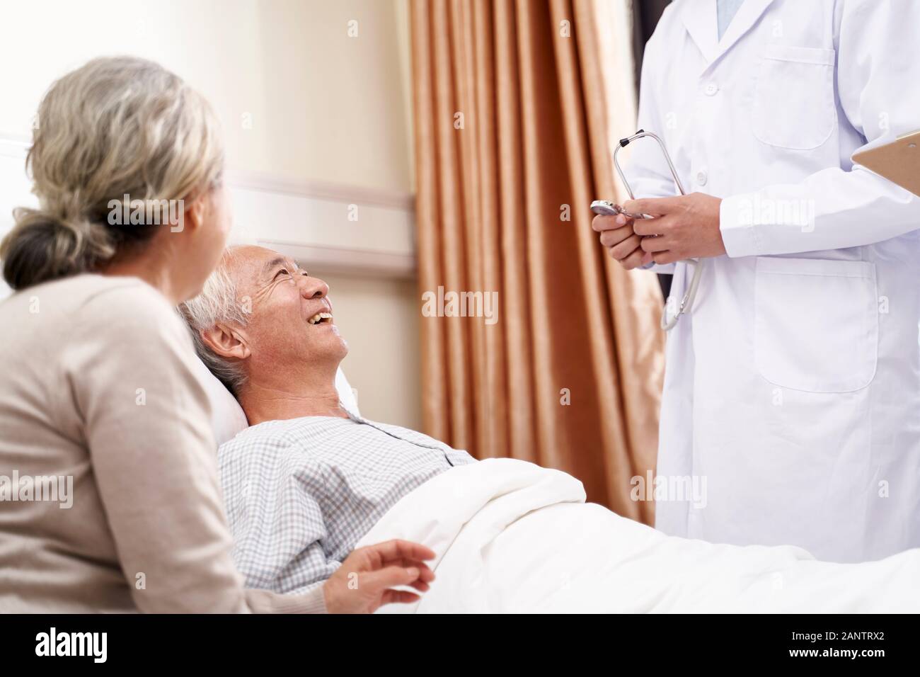 Senior asian man male patient lying on bed talking to doctor in hospital ward Banque D'Images