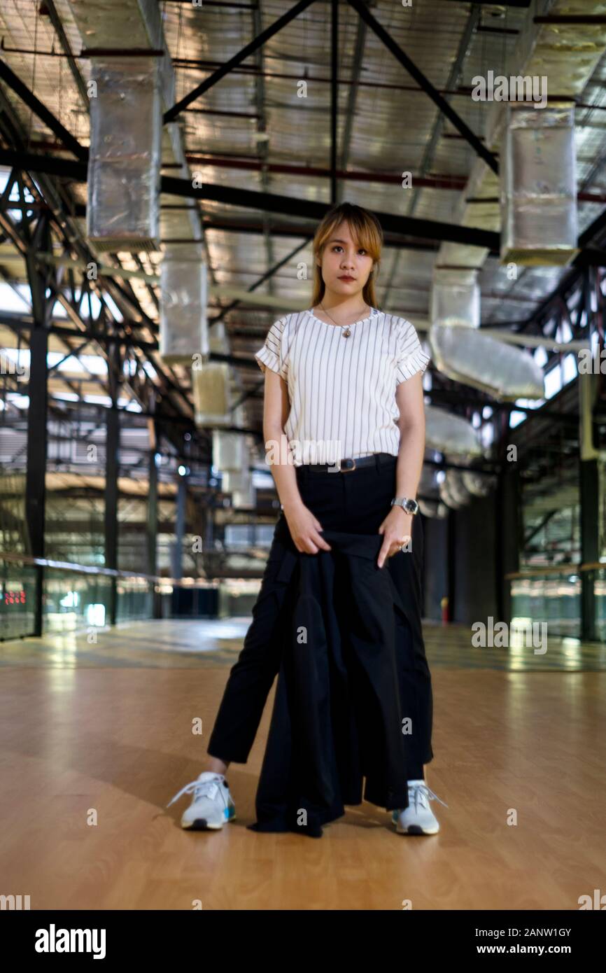 Femme aux cheveux blonds avec la moitié des cheveux attachés et permanent d'équilibre tenant son costume noir dans la voie de l'immeuble. Banque D'Images