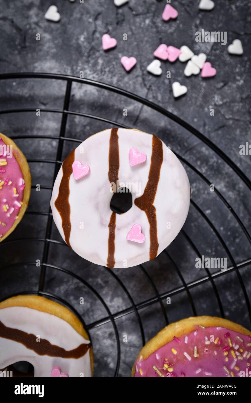 Vue de dessus du donut chocolat blanc avec vitrage en forme de coeur rose et saupoudre de sucre sur grille à gâteau Banque D'Images