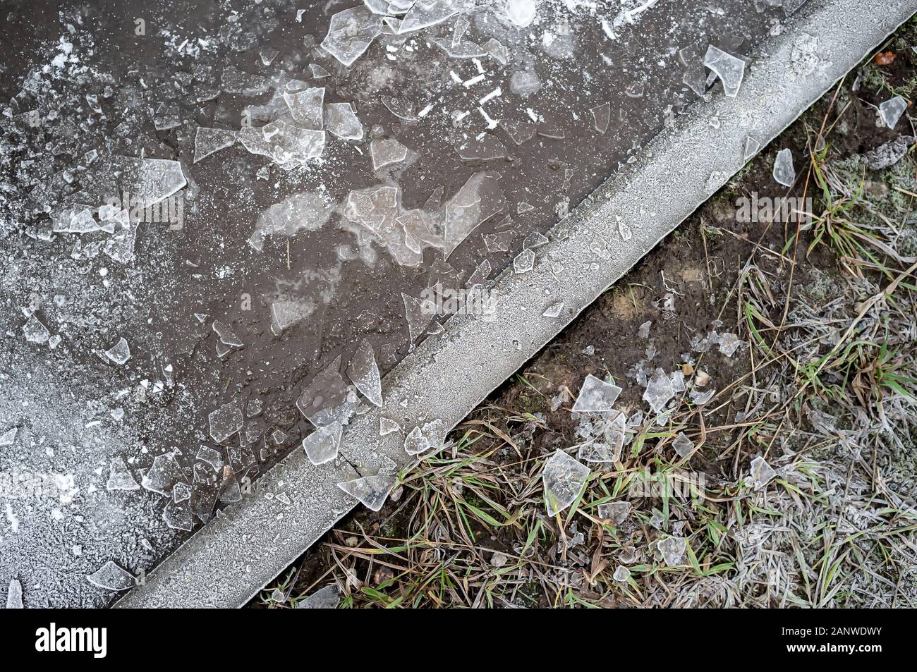 Flaque d'eau gelée avec des morceaux de glace, pelouse sèche couverte de givre et en divisant leur trottoir de l'hiver, un jour de grand froid. Banque D'Images