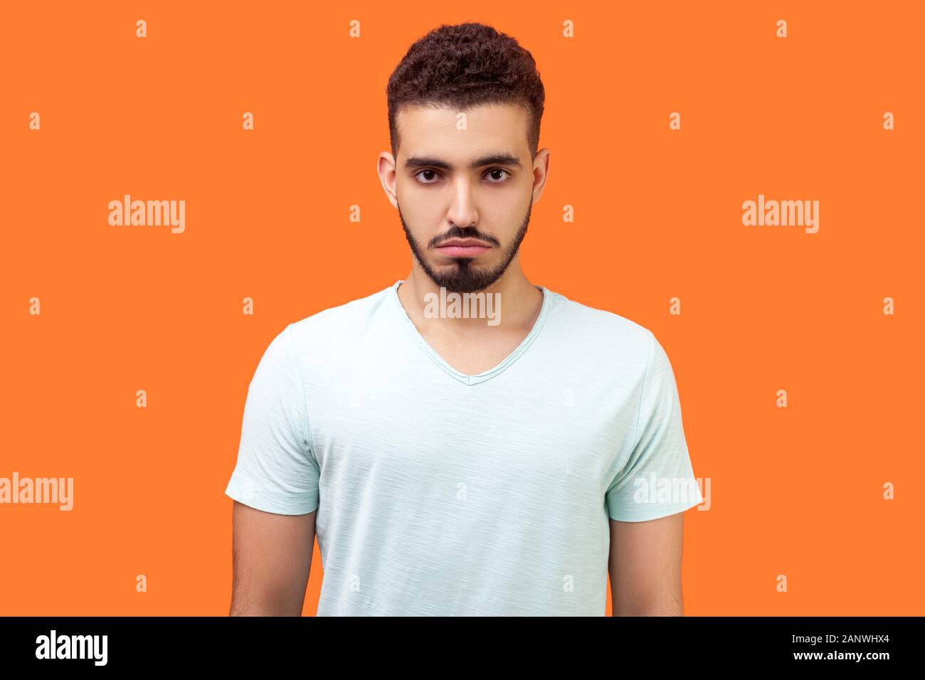 Portrait d'homme avec barbe brune en blanc occasionnels t-shirt looking at camera avec ressentiment insatisfait face expression, mauvaise humeur, dépression. Banque D'Images