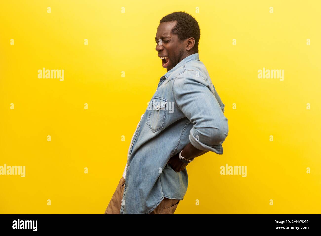 Portrait d'un jeune homme en denim chemise décontractée tenant la main à l'arrière avec grimace douloureuse, souffrant de Mal de dos ou l'inflammation des reins indo. Banque D'Images