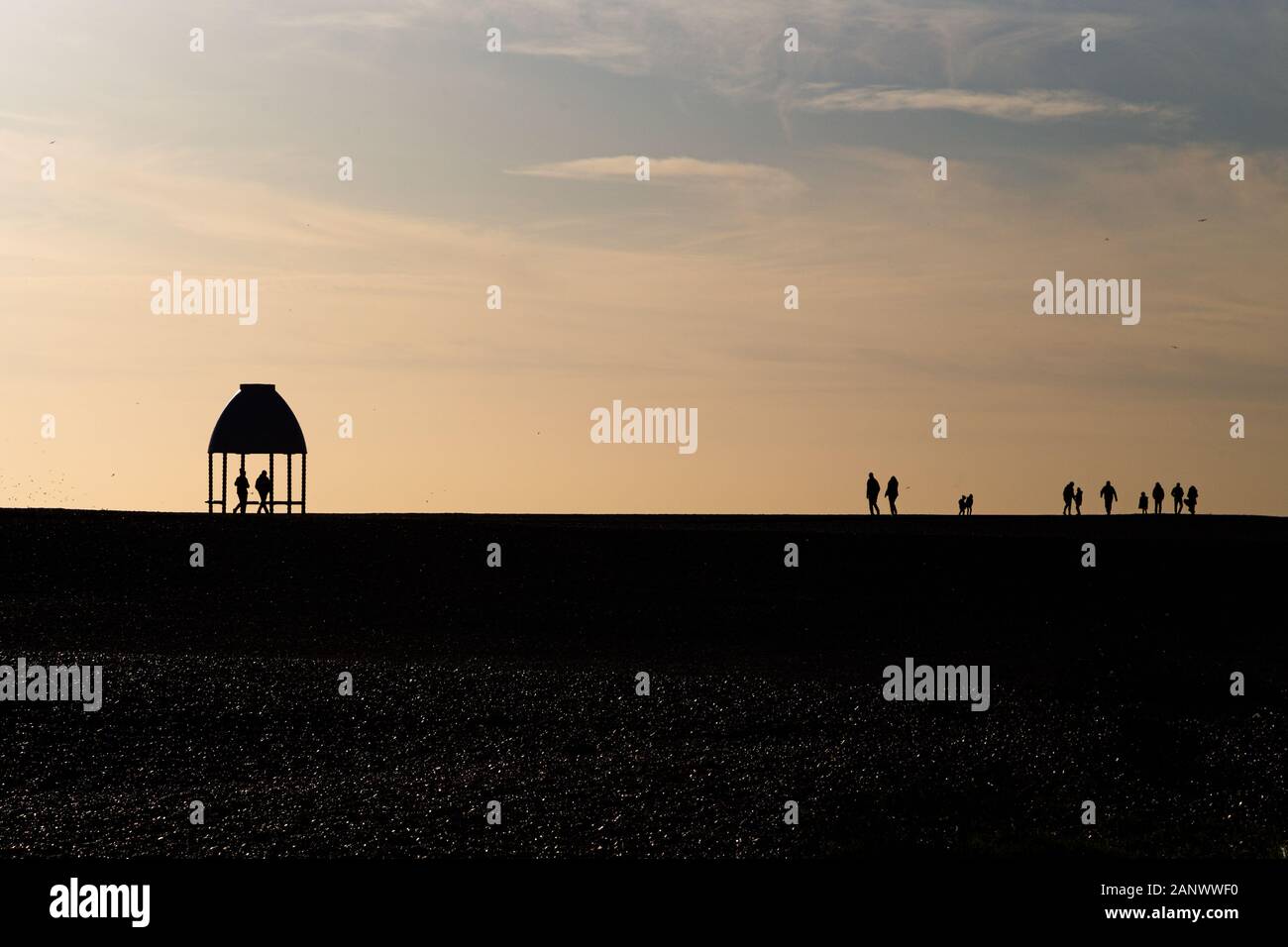 Folkestone, Kent. UK. Plage de galets à Coquelles avec des silhouettes de personnes dans la distance à la fin de l'hiver le soleil l'après-midi. Banque D'Images