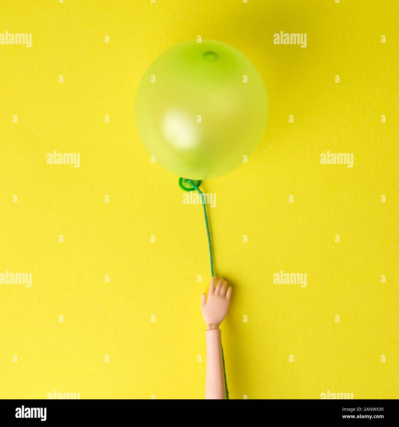 Doll hand holding balloon contre fond jaune un minimum de concept créatif. Banque D'Images