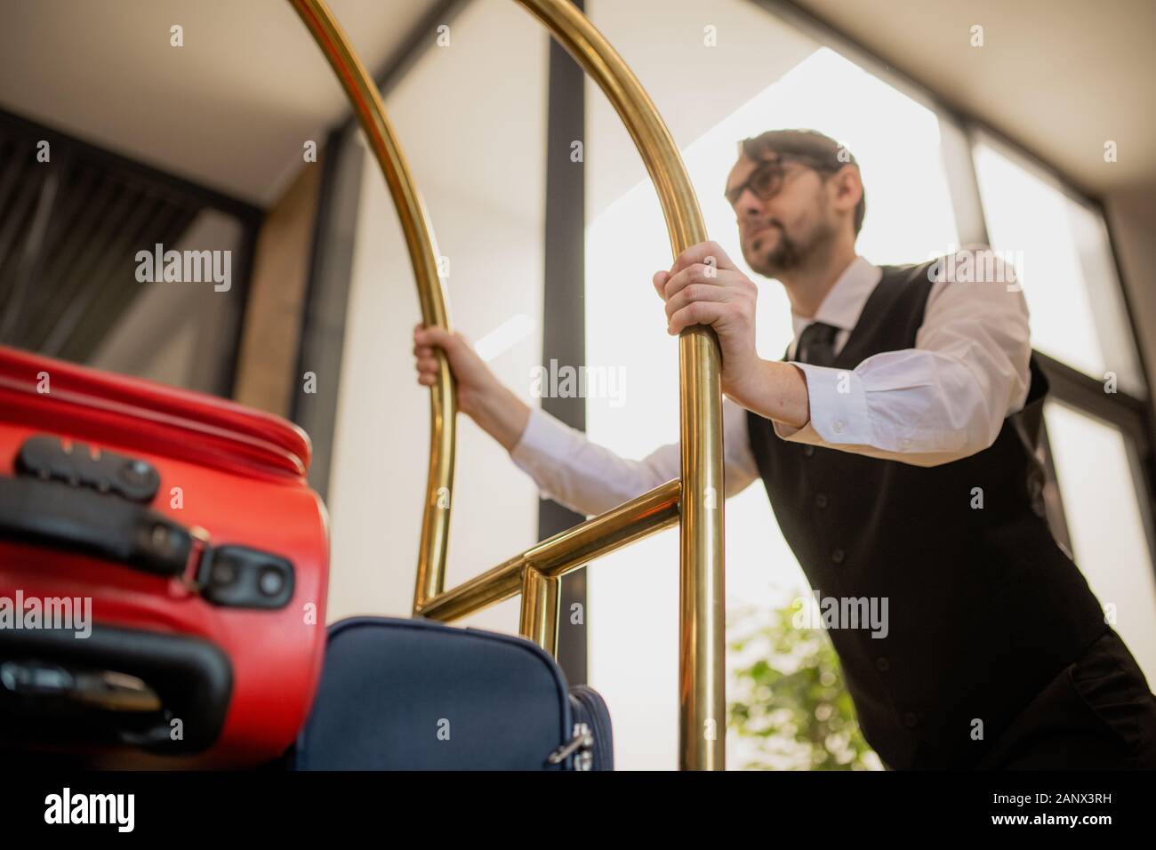 Porter contemporain par holding gère tout en poussant le panier avec des valises Banque D'Images