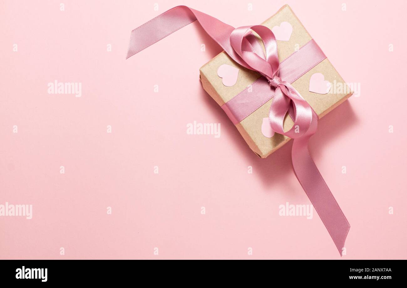 Boîte cadeau en papier brun avec un ruban violet arc et quatre coeurs roses sur elle sur fond rose sur le côté droit. Valentines Day concept. Télévision jeter top vi Banque D'Images