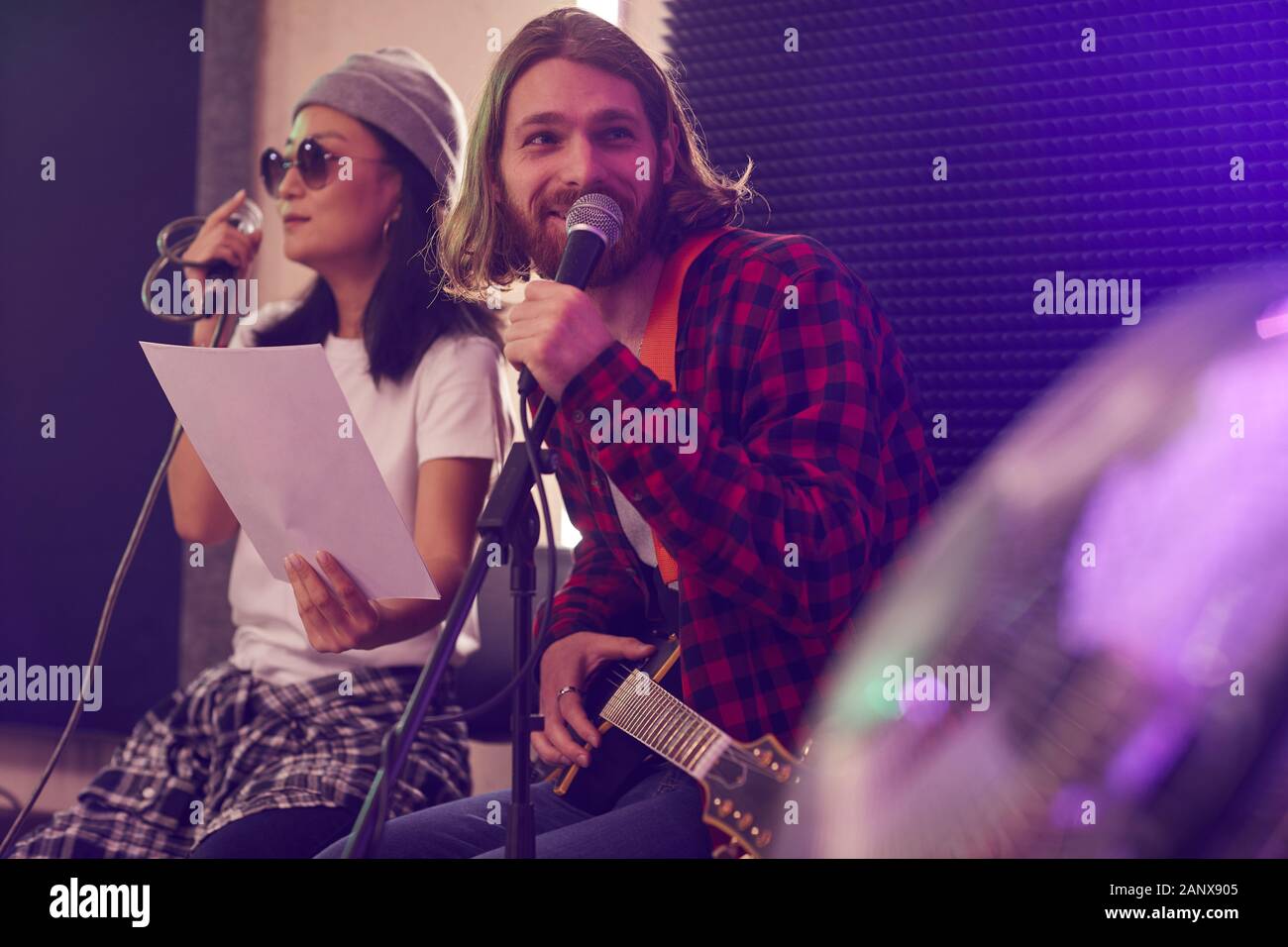 Portrait de jeune homme aux cheveux longs qui joue de la guitare et chanter au microphone en répétition ou concert avec music band de peu de lumière studio, copy space Banque D'Images