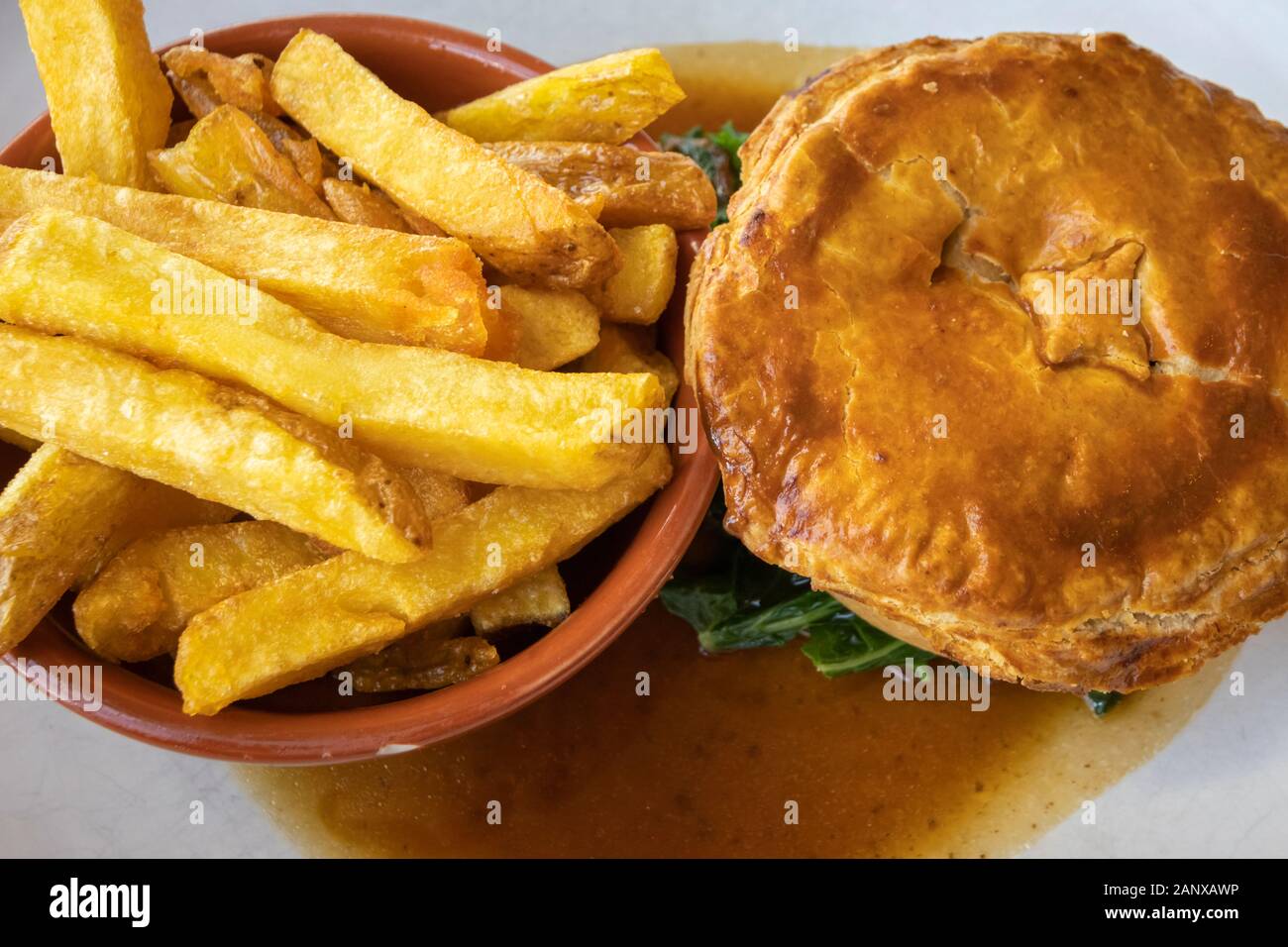 Copieux typique et savoureux repas au pub britannique : sex pâté à la viande en sauce servi avec un bol de golden fried chips chunky sur une plaque blanche chine Banque D'Images
