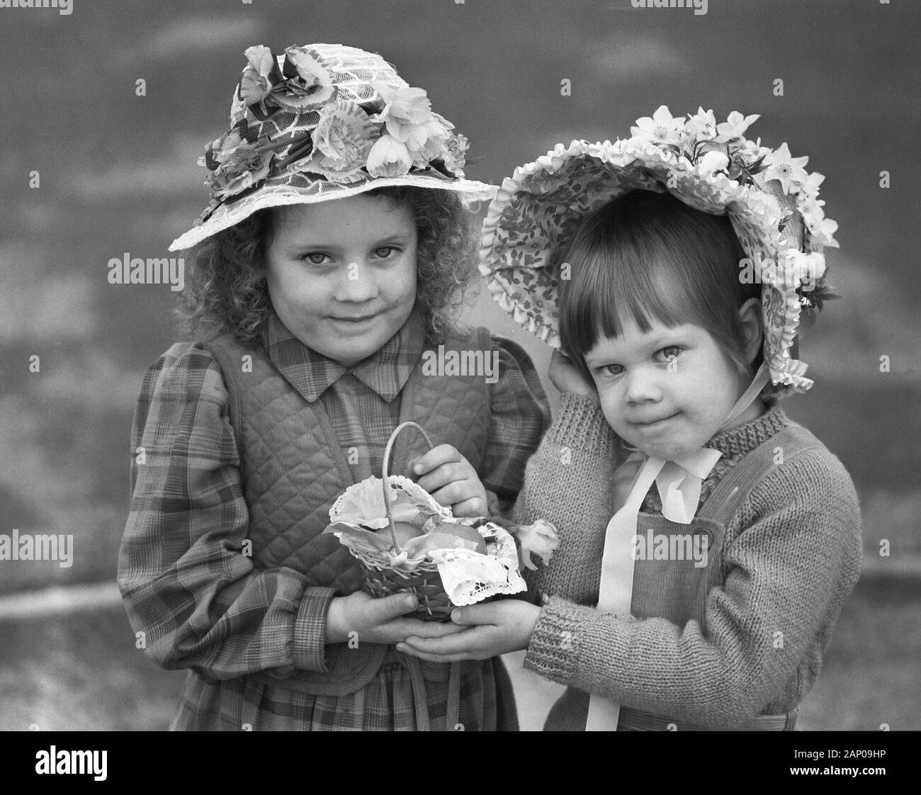 Années 1980, historiques, deux petites filles portant des bonnets de pâques et tenant un petit panier de Pâques, England, UK. La tradition de porter un chapeau à Pâques vient du désir d'celebratethe venue du printemps et la signification de pâques pour les chrétiens. Banque D'Images