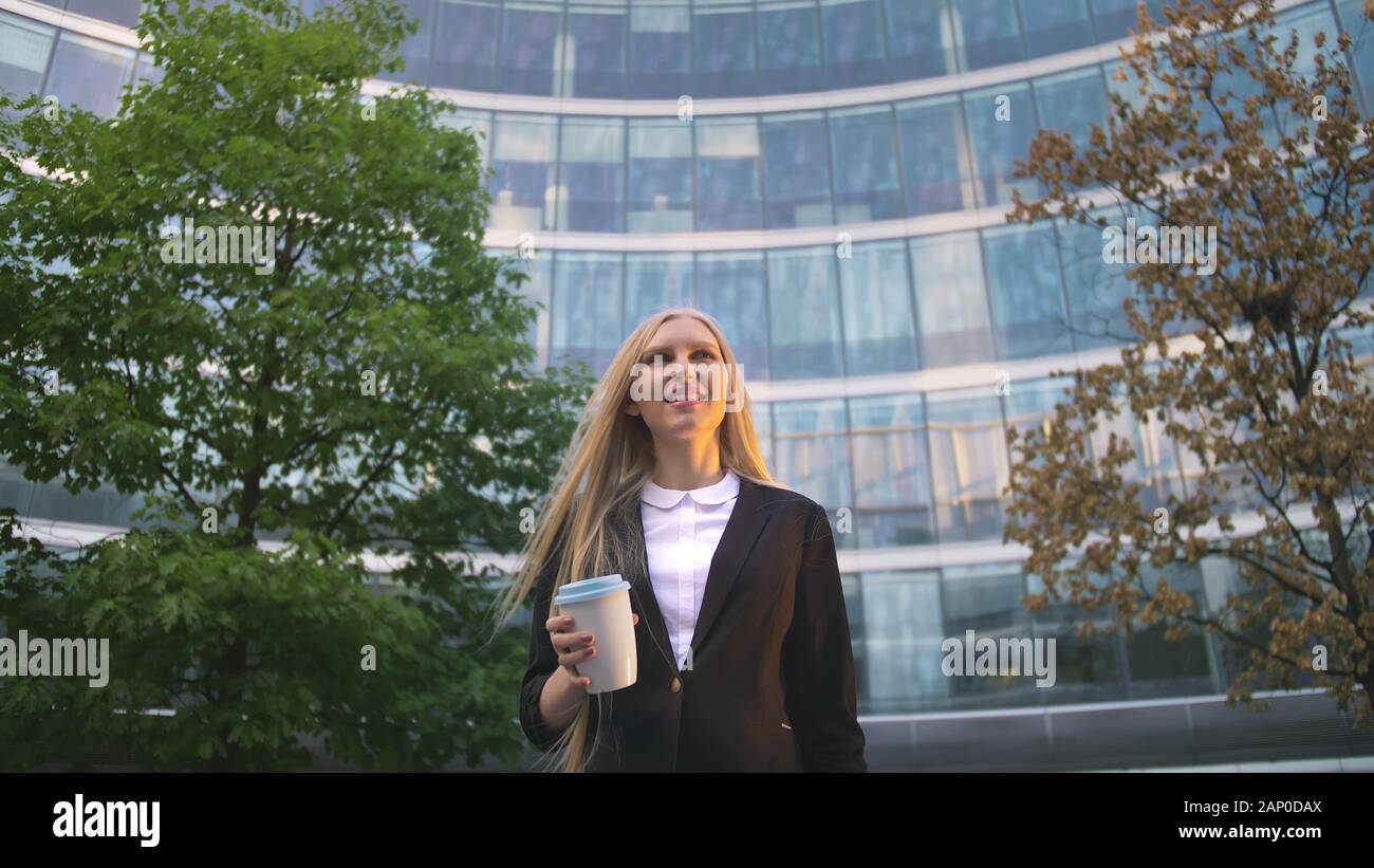 Par en dessous de la blonde woman in suit le café dans la tasse de papier à l'écart sur rue. Banque D'Images