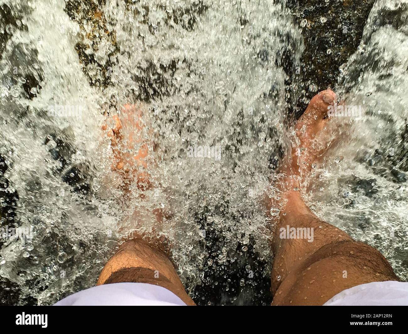 Le pied des deux pieds qui se trouvent dans la cascade qui coule JusQu'À ce que l'eau se scinde en granules Banque D'Images