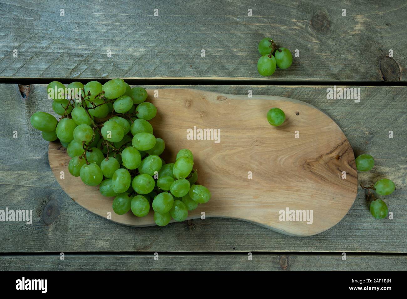 raisins blancs sur une plaque en bois. La plaque est sur un fond en bois. Banque D'Images