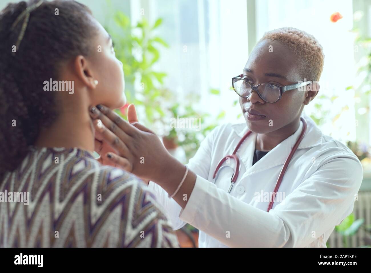 Petite fille africaine dans une couche de blanc, avec un phonendoscope, porter des lunettes, examine une jeune fille mexicaine de patient avec un mal de gorge. Le concept de l'amygdalite, s Banque D'Images