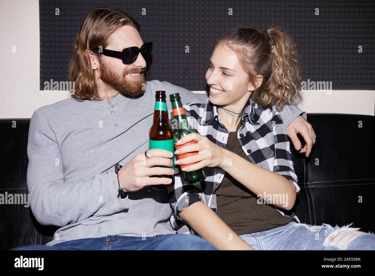 Portrait du jeune couple moderne cliquetis de bouteilles de bière tout en profitant d'une discothèque, tourné avec flash Banque D'Images