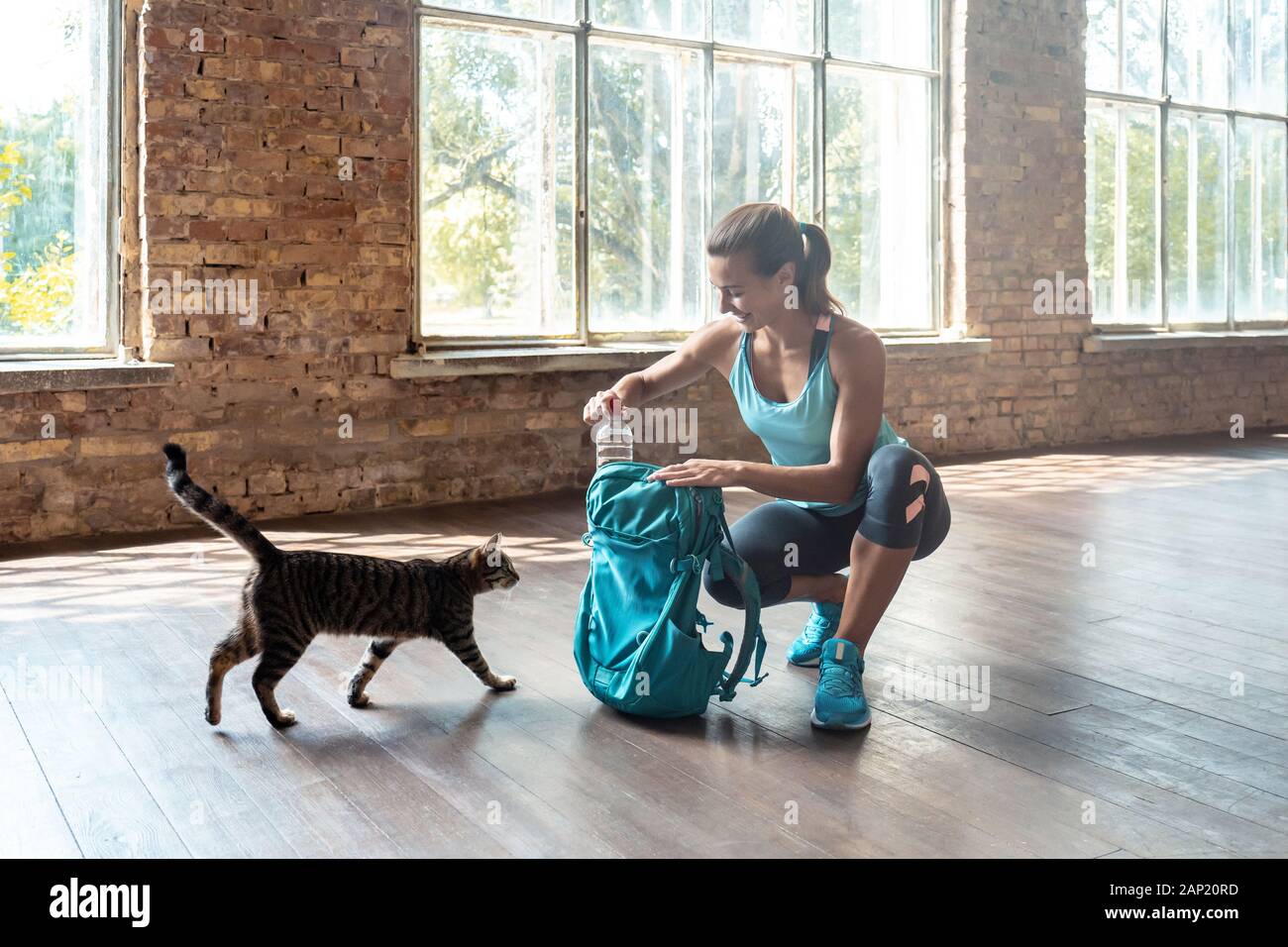 Jeune femme sportive heureuse déballer un sac à dos de sport moderne jouant avec chat drôle Banque D'Images