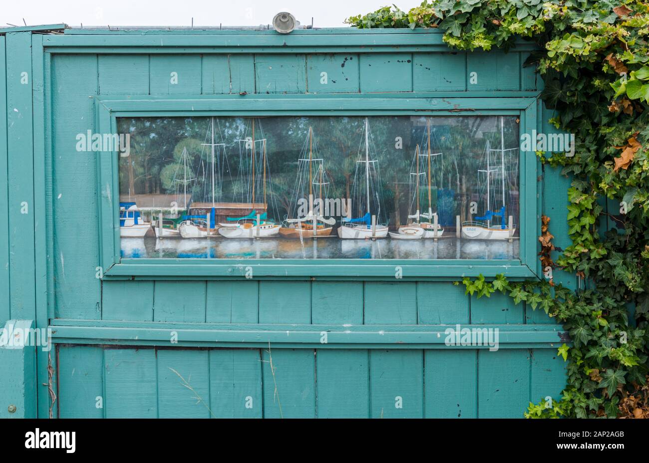 Une peinture de voiliers dans un port bordé d'arbres est affichée sur une clôture verte dans la ville de Morro Bay, sur la côte californienne Banque D'Images