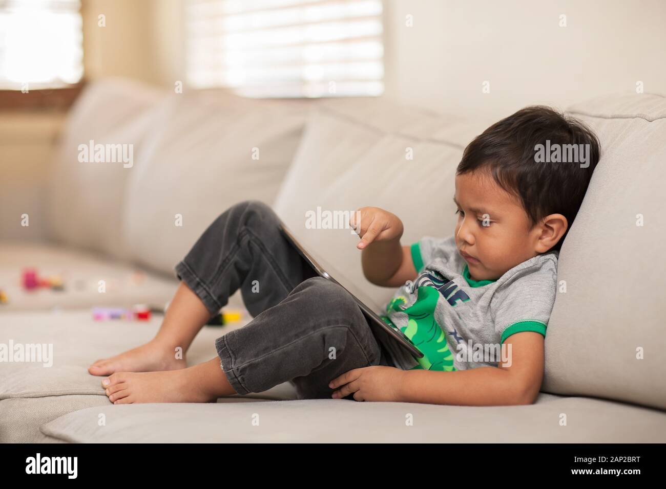 Détente sur un canapé à la maison, un enfant utilise son doigt pour interagir avec une tablette graphique qu'il utilise. Banque D'Images