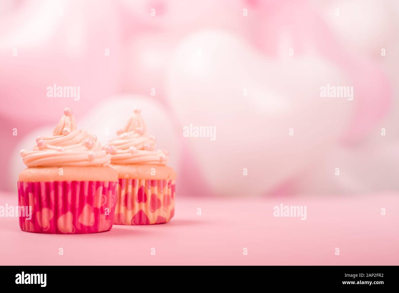 Deux saint valentin love cupcakes décorés avec de la crème sur la partie rose et blanc ballons coeur fond avec copie espace pour le texte Banque D'Images